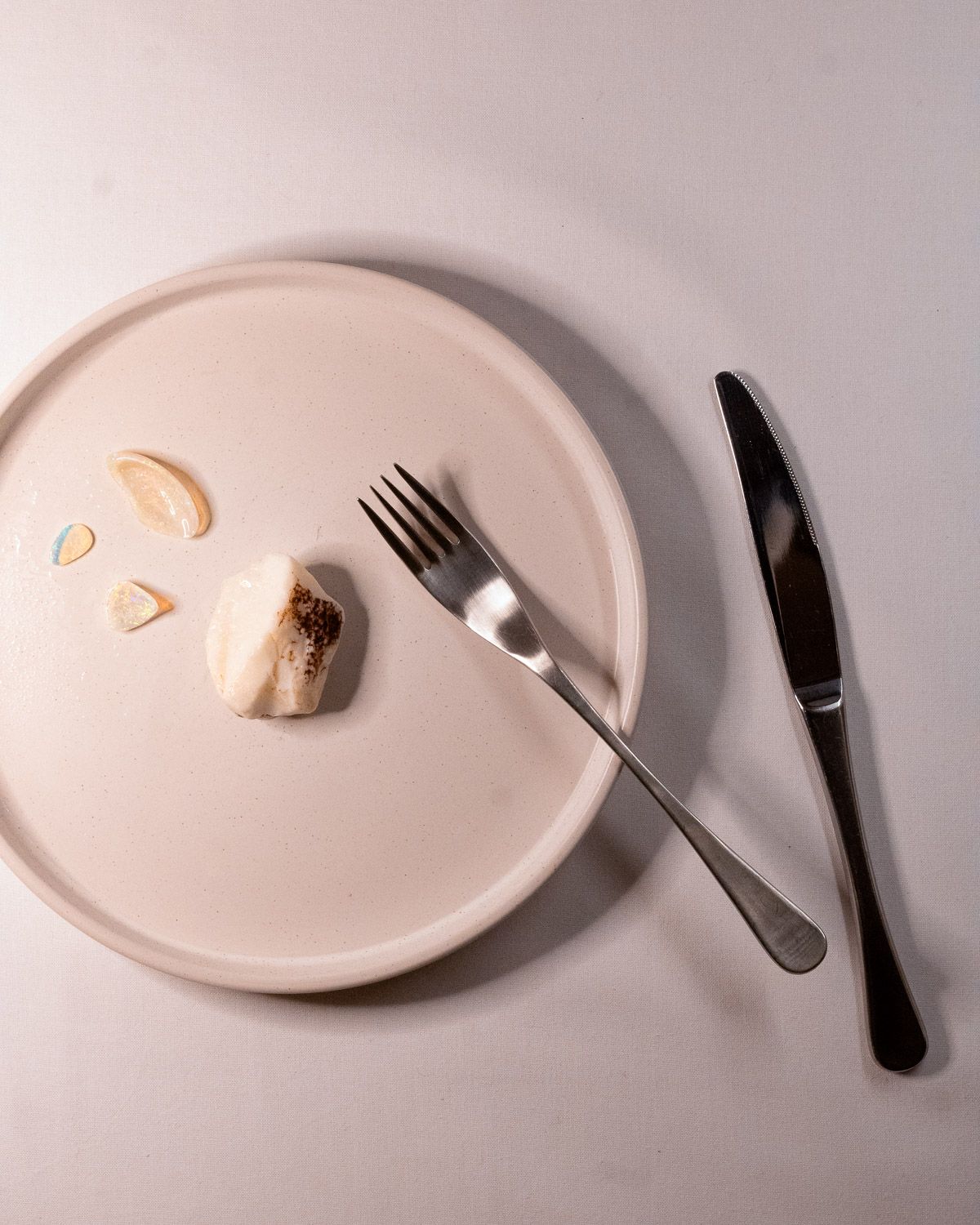 Opal No. 005 on a pale ceramic plate with a fork, knife and small opal pieces