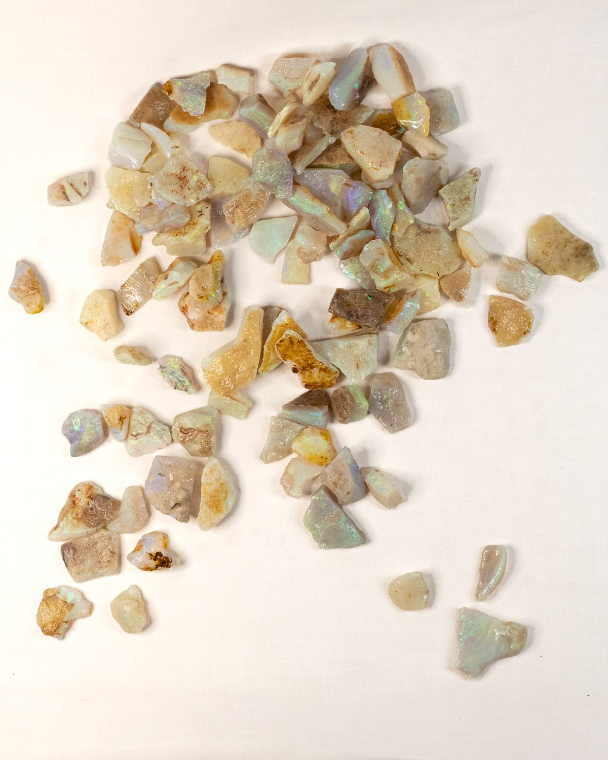 Opal No. 020, a large lot of small raw opal pieces scattered on linen